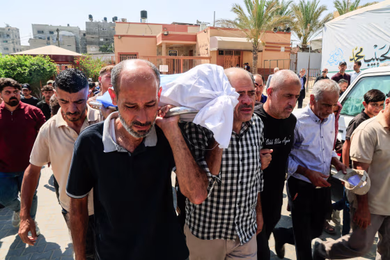 Mourners carry a body covered in white tarp outside