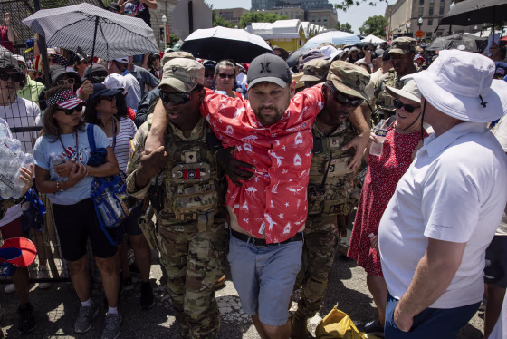 Two soldiers in camouflage help carry a man through a crowd.