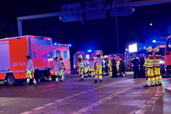 Emergency workers in fluorescent safety gear in front of ambulances at night.