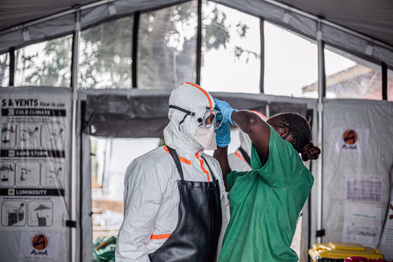 A hygiene worker helps a doctor put on personal protective equipment inside of a room