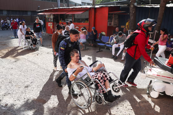 People in wheelchairs are assisted outside, while others sit in waiting room chairs that have been placed outside