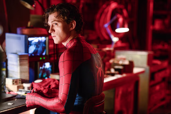 Tom Holland wearing a Spider Man suit and sitting at a work desk