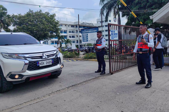 Security guards stand by a gate while a car stads next to them.
