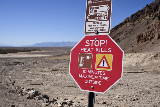 A red sign reading STOP! HEAT KILLS in a desert landscape.
