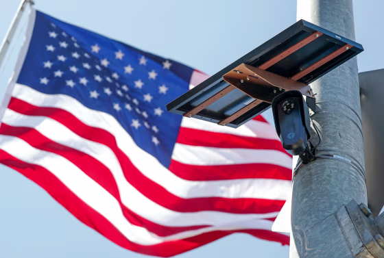 An American flag flies behind a Flock Safety camera tmounted to a light pole