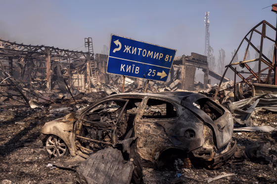 A burned car sitting in the midst of further wreckage after an explosion.
