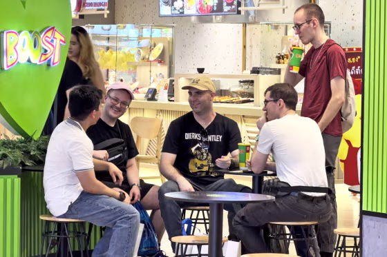 Image: A group of men sat at a juice bar table smiling and talking.