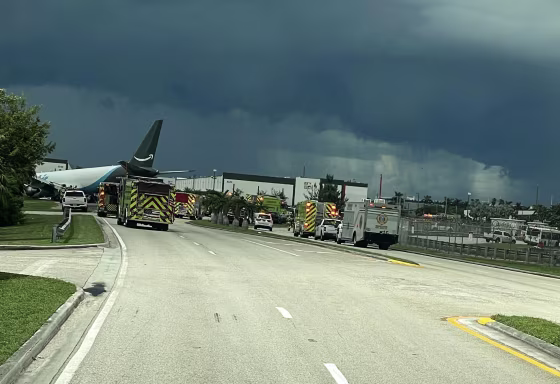 Emergency vehicles gathered near a jet at an airport under stormy skies.