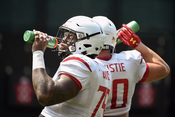 Two football players drinking from green water bottles in their red and white uniforms.