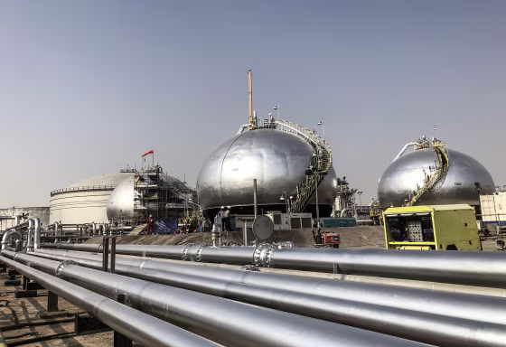 Round metallic storage tanks and pipelines in a desert landscape.