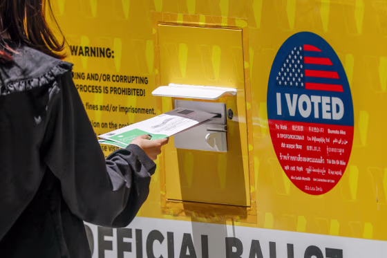 A person places their Mail in ballot into a ballot box.