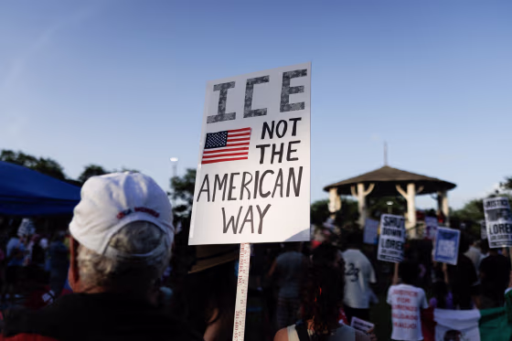 A man holds a sign reading ICE NOT THE AMERICAN WAY.