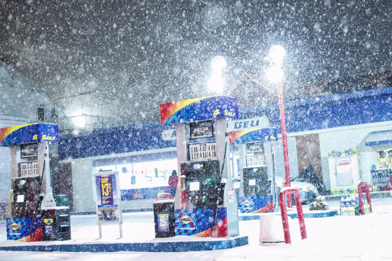 Snow falls by a gas station.