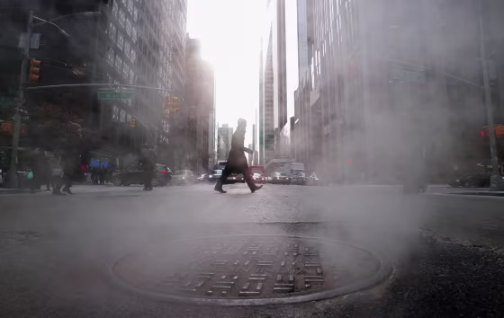 Steam rises from a sewer as a man crosses the street.