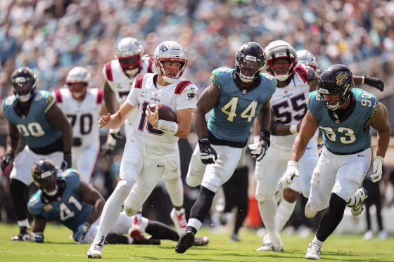 Drake Maye running the football in front of several Jaguar defenders.