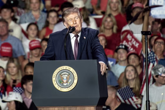 Donald Trump speaking at a podium with the presidential seal during a rally.