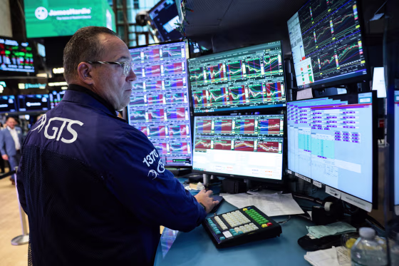 A trader looks at multiple computer screens at a desk