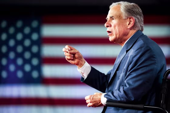 Greg Abbott speaks on stage, an American flag backdrop is seen in the background