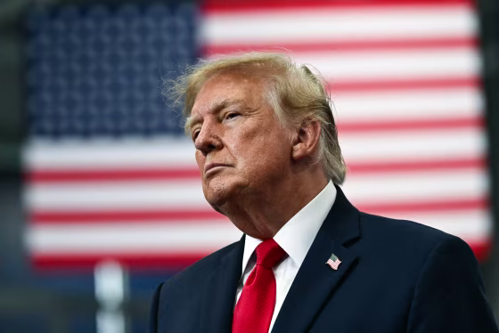Donald Trump stands in front of an American flag backdrop