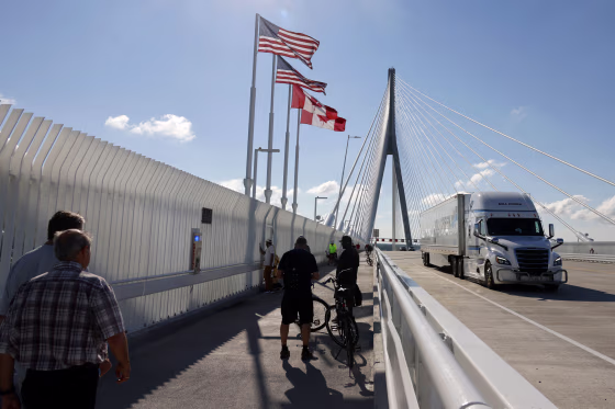 A freight truck drives over a bridge decorated with American and Canadian flags.