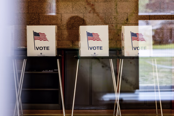 Three voting booths seen through a reflective window.