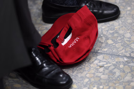A red MAHA hat lying on the floor between a person's feet.