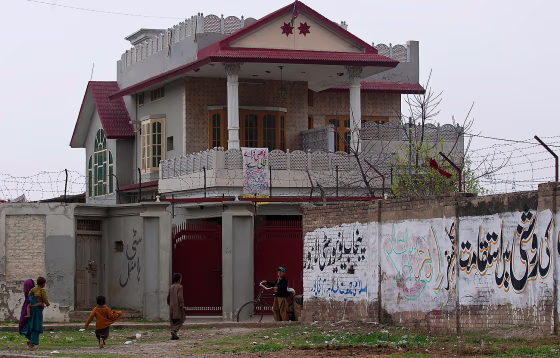 In this photo taken Thursday, March 8, Afghan refugees gather outside a house in Haripur, Pakistan, that Pakistan's intelligence agency believes Osama bin Laden lived in for nearly a year until he moved into the villa where he was eventually killed.  The home in the frontier town of Haripur was used by bin Laden while he waited for construction crews to finish his new home in the garrison town of Abbottabad, just 18 miles away. The graffiti at right reads, "journey with persistence in light and congregation in Punjab Universality Lahore called by an Islamic students group Islami Jamaiat Tulba, Haripur."