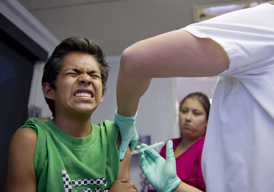 Public school student Julio Valenzuela, 11, grimaces as he gets a vaccination at a free immunization clinic for students before the start of the schoo...