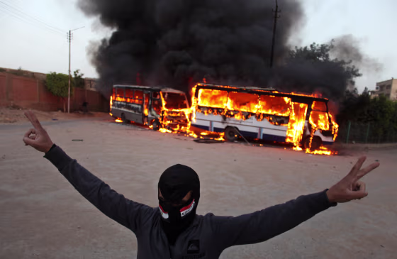 A masked protester flashes the victory sign as he stands in front of burning buses during clashes between supporters and opponents of Egypt's powerful Muslim Brotherhood near the Islamist group's headquarters in Cairo, Egypt&nbsp;on March 22, 2013.