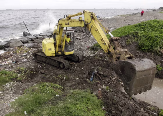 A Filipino government worker operates a backhoe to reinforce a flood control barrier in Pasay city, south of Manila, Philippines, Friday.