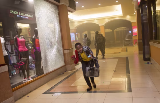 A woman who had been hiding during the gun battle runs for cover after armed police, seen behind, enter the Westgate mall in Nairobi, Kenya, on Saturday. The Somalia-based terrorist group al-Shabab claimed responsibility for the attack.