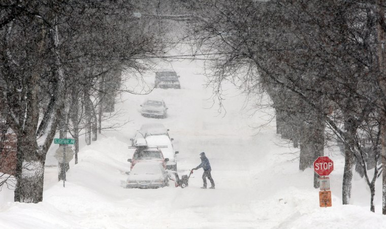 Image: A man uses a snowblower to clear snow from his car after snowfall in Minneapolis