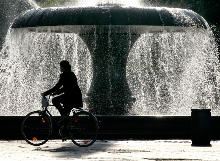Image: A woman cycles near a fountain in Frankfurt