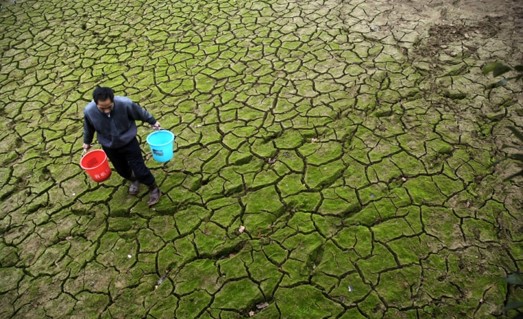 Image: A farmer carries pails to transport water from a partially dried-up pond
