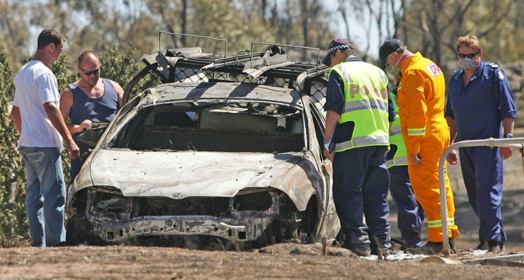 Image:  Police oficers examine the remains of a burnt out vehicle