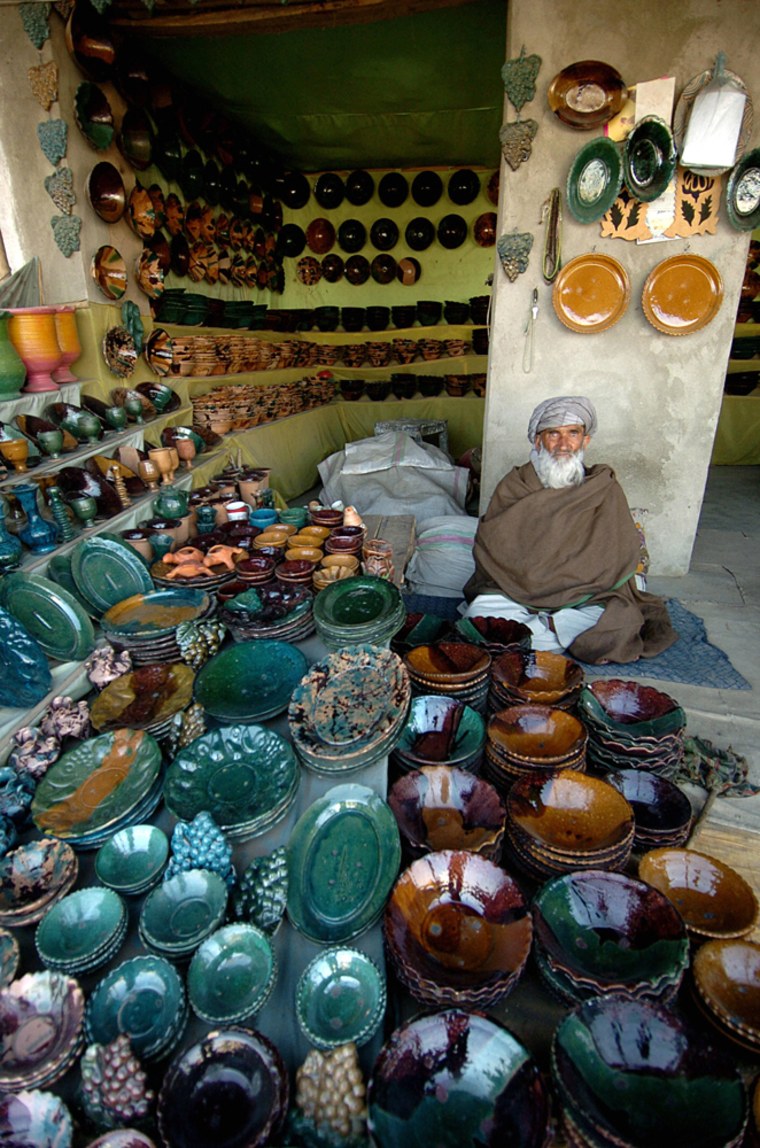 Image: An Afghan potter displays his wares at the artisan's village of Istalif