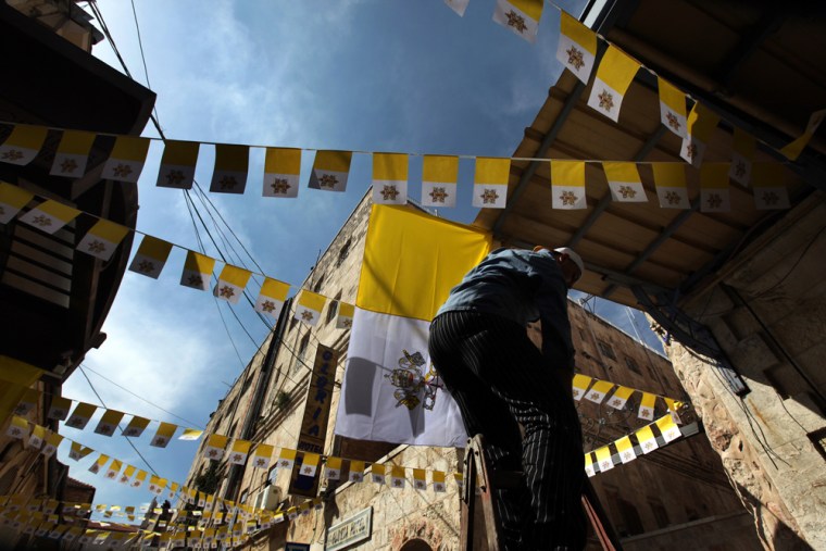 Image: A Palestinian man decorates a street with Vatican flags in the old city of Jerusalem