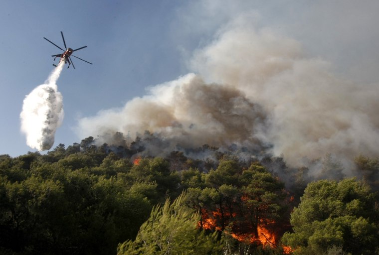 Image: A fire-fighting helicopter drops water over a forest fire in Nea Makri village northeast of Athens