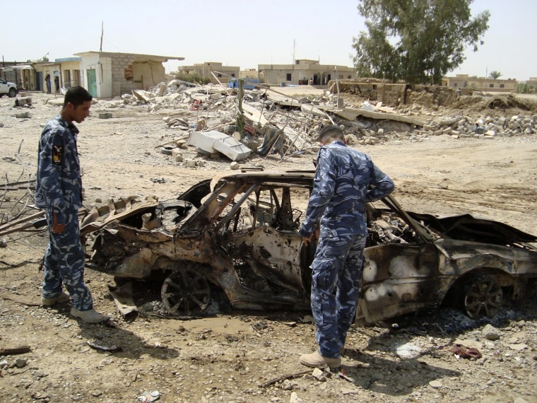 Image: Iraqi policemen inspect the wreckage of a vehicle used in a car bomb attack in Shirqat