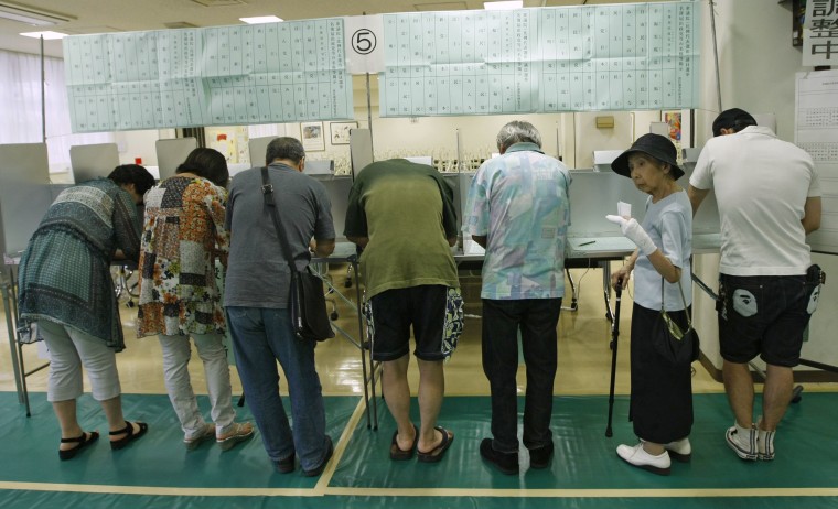 Image: People fill out ballots for the lower house election at a polling station in Tokyo