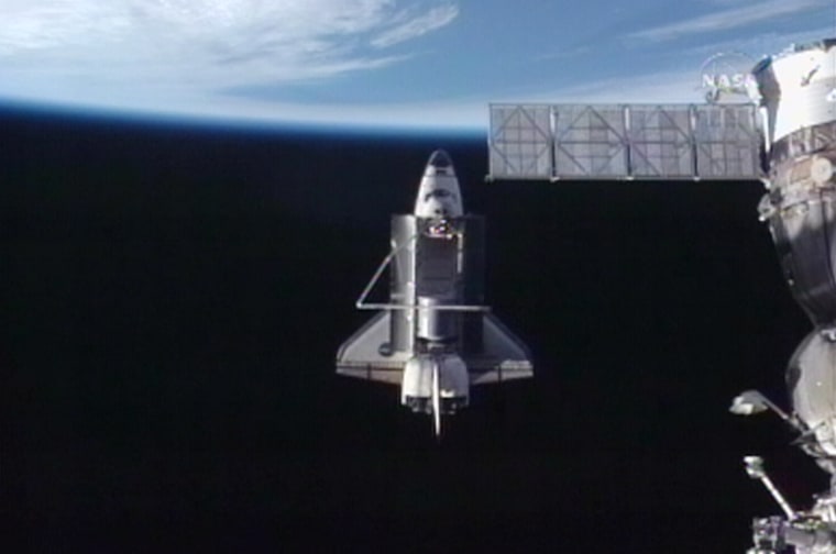 The space shuttle Discovery pulls away from the international space station on Tuesday, with part of a Russian transport ship visible in the foreground and Earth looming in the background.