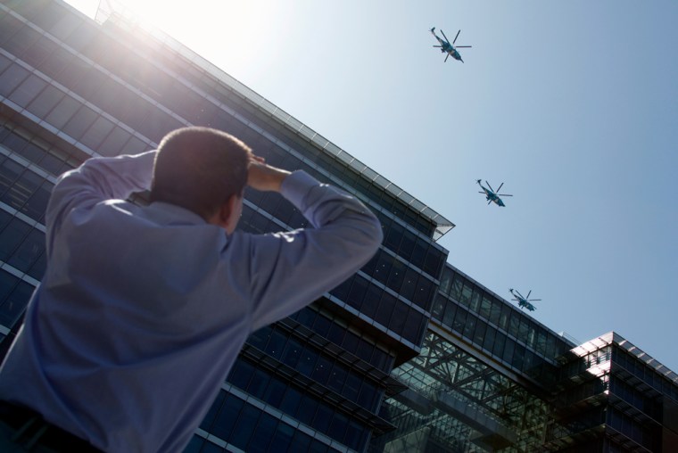Image: Office worker looks up at Chinese Air Force helicopters as they fly over a building near Beijing's Tiananmen Square during a rehearsal for the National Day parade