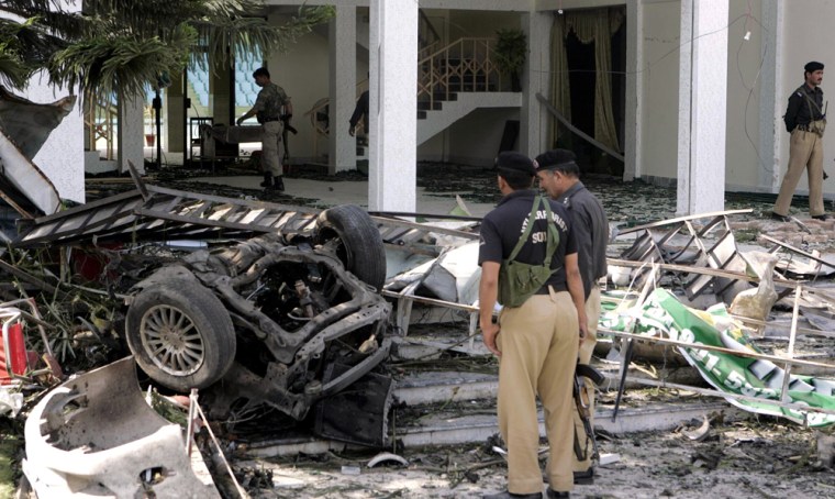 Image: Pakistani police officers examine the wreckage of a car at the site of a bomb explosion