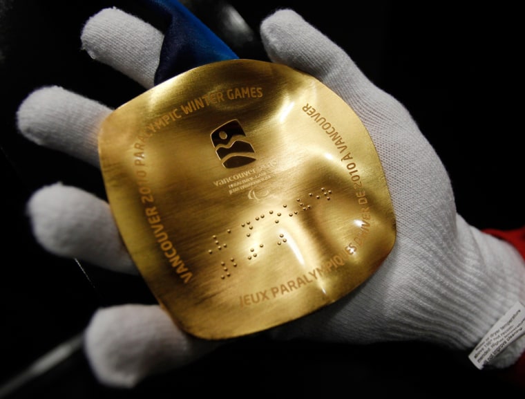 Image: A visitor to the Royal Canadian Mint displays a replica of a Paralympic gold medal featuring Braille script on the second day of the Vancouver 2010 Winter Olympics
