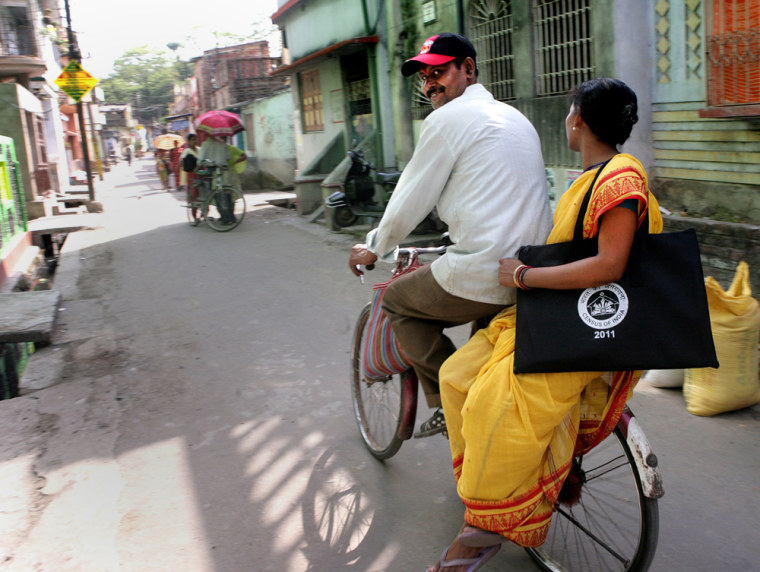 Image: An Integrated Child Development Service staff member sits on a bicycle as she returns home with the documents she need for her role as census-taker at Halisahar village