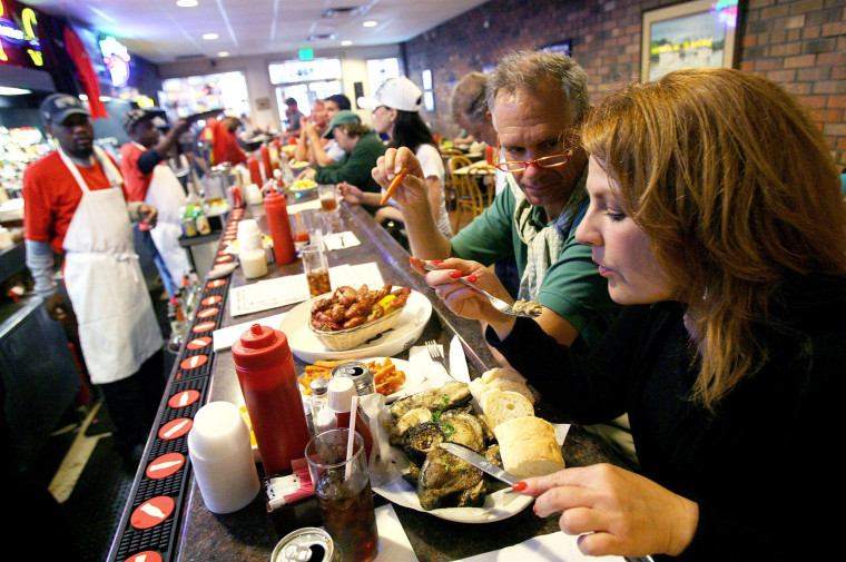 Image: Kelsey of Boston, Massachusetts blows hot \"Charbroiled Oysters\" at Felix's Seafood Restaurant in New Orleans