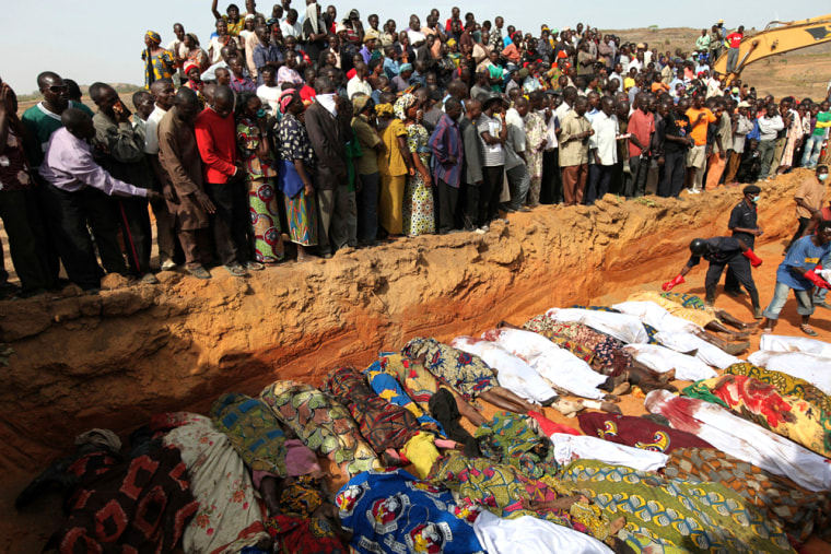 Image: Villagers look at bodies of victims of religious attacks lying in a mass grave in the Dogo Nahawa village