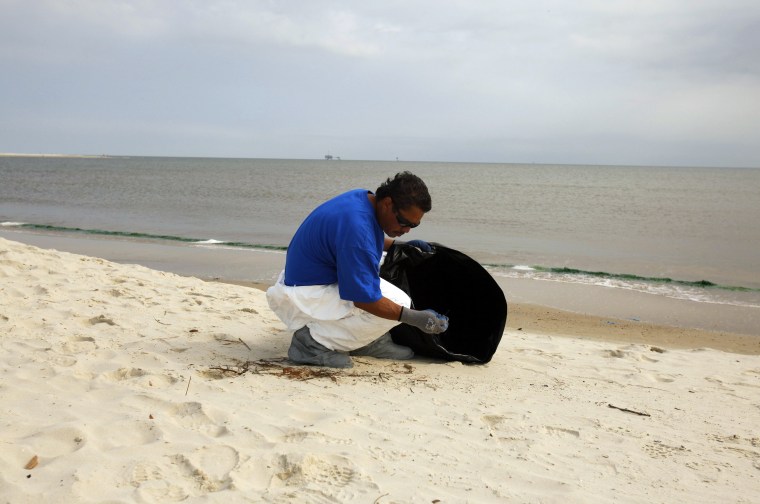 Image: A clean-up crew member collects tar balls at Dauphin Island, Alabama
