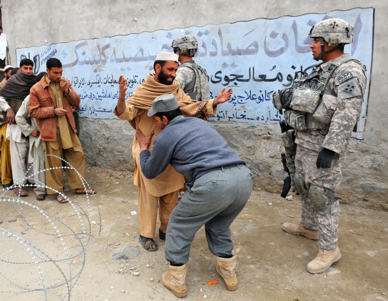 image: An Afghan policeman frisks a man at a security checkpoint