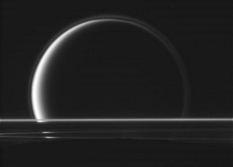 This rare picture shows the edge of Enceladus' dark disk at bottom foreground, the rings of Saturn just above, and the crescent disk of Titan in the background.